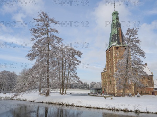 Castle with high tower in winter. Snow-covered trees and a frozen lake in the foreground, Raesfeld, münsterland, germany