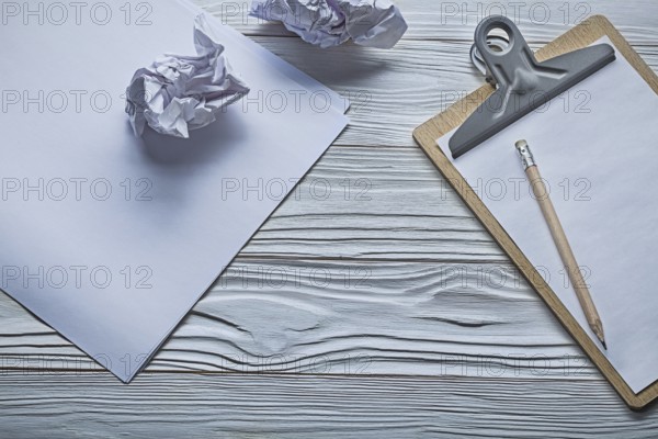 Crumpled paper balls and small clipboard with pencil on vintage white wooden boards