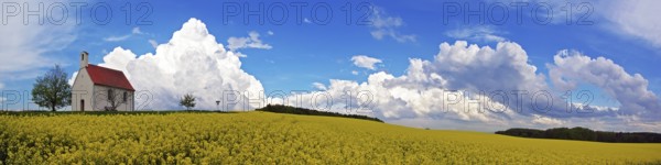 Panorama, chapel and storm clouds over a rapeseed field