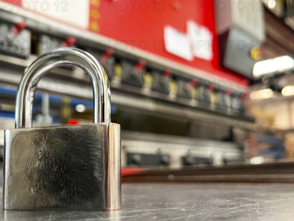 Image of a metal padlock in the foreground against the background of a metal bending machine. Concept of safety at work