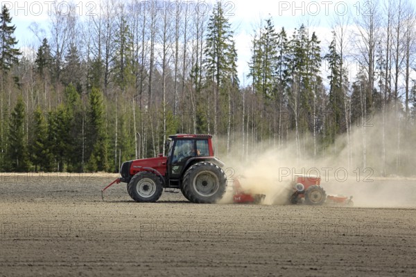 SALO, FINLAND, MAY 7, 2017: Farmer cultivates field with red Valtra tractor and seed drill surrounded by dust on a clear day of spring in South of Finland