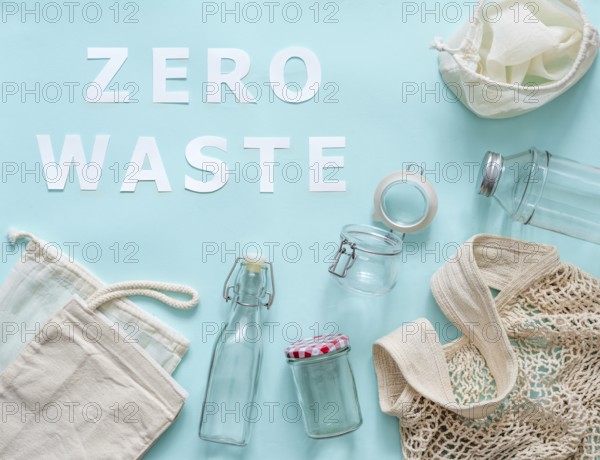 Zero waste concept. Textile eco bags, glass jar and bottle on blue background with Zero Waste white paper text. Eco friendly and reuse concept. Top view or flat lay