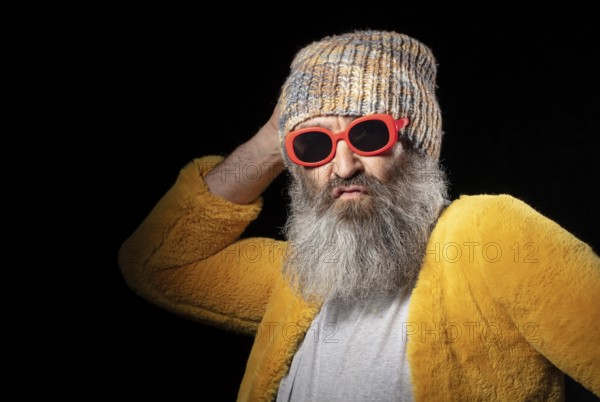 Creative older man with grey beard in fashionable clothes on black background