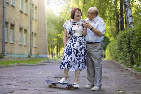 Happy elderly couple with a skateboard. Handsome man and woman seniors. Husband and woman in old age for a walk in the city