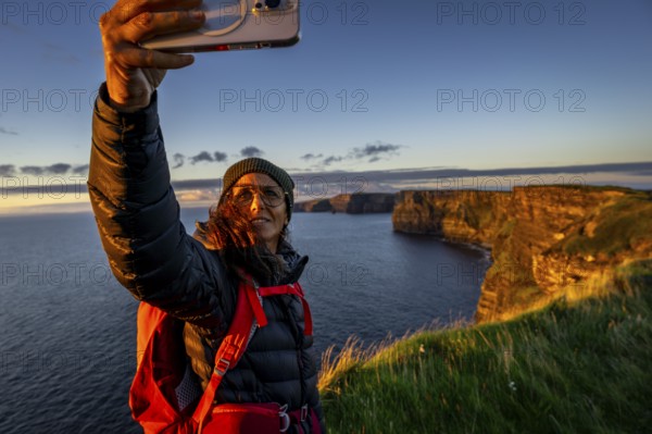 Female hiker taking a selfie, Cliffs of Moher, The Burren, County Clare, Ireland, United Kingdom, Europe
