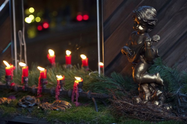 A golden angel figure next to a row of burning red candles on moss, borken, münsterland, germany
