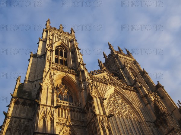 A front view of the towers at the entrance to york minster in sunlight against a blue cloudy sky