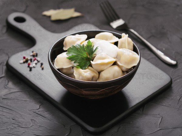 Traditional russian pelmeni, ravioli, dumplings with meat on black cutting board over black concrete background. Russian food and russian kitchen concept