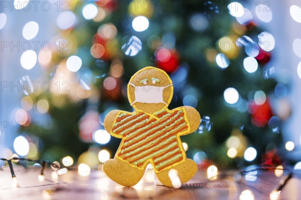 Gingerbread man in a protective icing mask on the table in the light of multi-colored lights on the Christmas tree. Blur.
