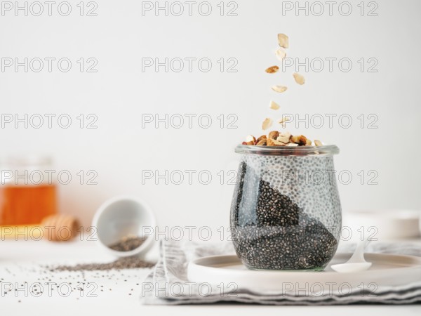 Healthy breakfast concept and idea - two colors chia pudding with organic raw almond. Glass jar with black charcoal and white vegan milk chia pudding with falling chopped almond. Copy space