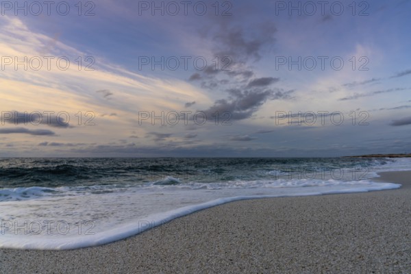 A low angle view of white sand beach with waves rolling in under a colorful sunset sky