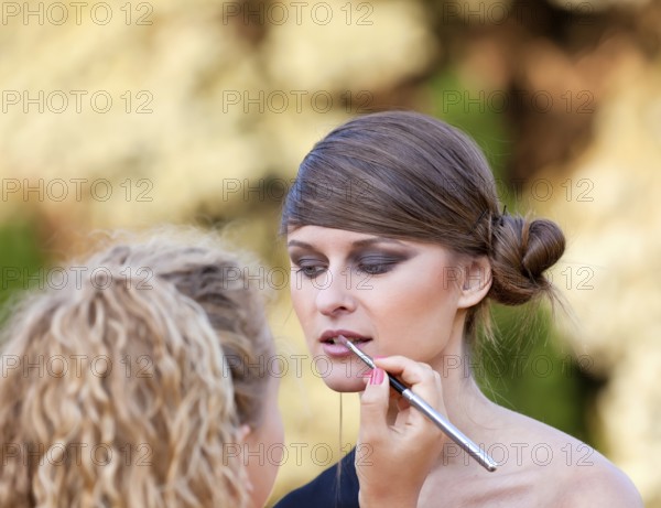 Makeup master applying lipstick with brush on caucasian girl lips