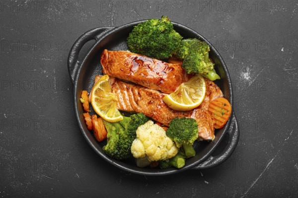 Healthy baked fish salmon steaks, broccoli, cauliflower, carrot in cast iron casserole bowl black dark stone background. Cooking a delicious low carb dinner, healthy nutrition, food photography