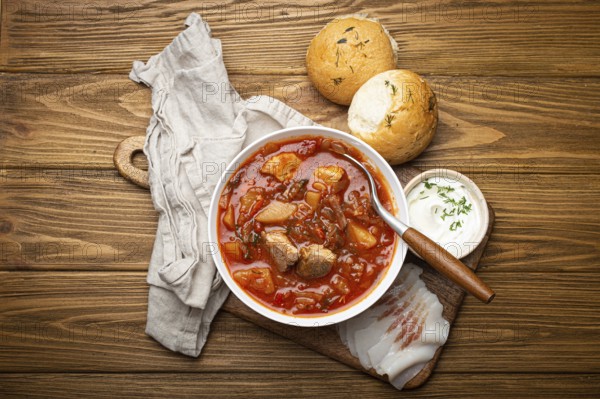 Ukrainian Borscht, red beetroot soup with meat, in white bowl with sour cream, garlic buns Pampushka and salo slices on rustic stone background. Traditional authentic dish of Ukraine, food photography, food photography