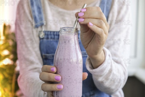 Female hands holding Blueberry smoothie topped with blueberries. Woman eating glass of breakfast protein smoothie drink made from pureed raw blueberries, banana, milk, yogurt, and cottage cheese. Vegetarian vegan food