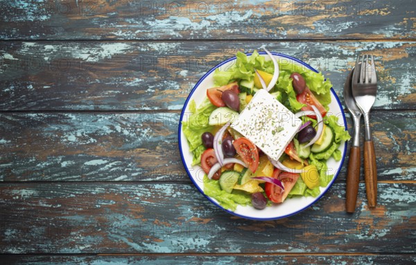 Traditional Greek Salad with Feta Cheese, Tomatoes, Bell Pepper, Cucumbers, Olives, Herbs in white ceramic bowl on blue rustic wooden table background from above, Cuisine of Greece. Space for text, food photography, food photography
