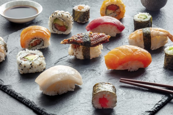 Sushi with chopsticks. Rolls, maki, nigiri on a black background, Japanese food. Salmon, tuna, eel, shrimp and other seafood with rice on a plate at an Asian restaurant, Food photography, Food photography