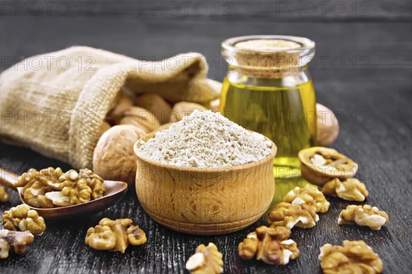 Walnut flour in bowl, nuts on a table, in a spoon and in a bag, oil in glass jar on wooden board background