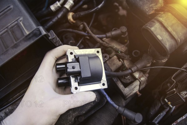 Hand holds car part with engine components around, highlighted by warm lighting