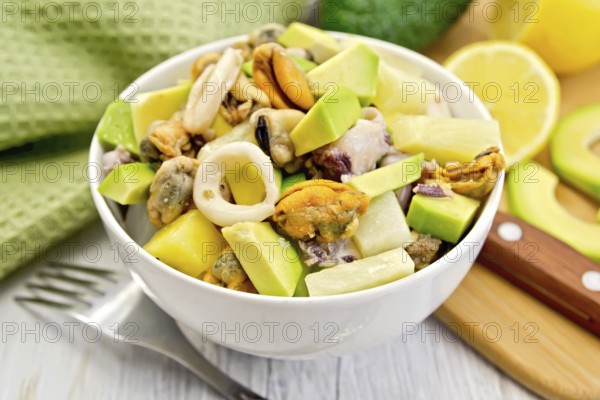 Salad with shrimps, octopus, mussels and calamari with avocado, lettuce, lemon and pineapple in a bowl, napkin on the background light wooden boards