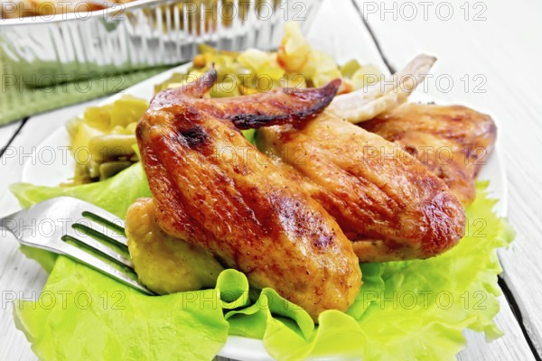 Fried chicken wings with vegetables and salad leaves on a plate, fork on the background light wooden boards