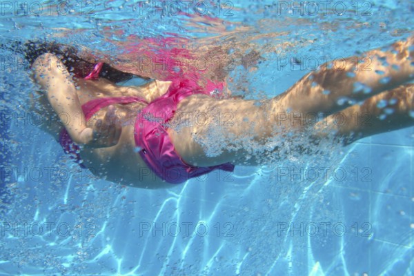 Underwater pink bikini little girl swimming in blue pool