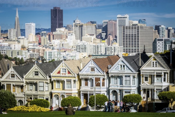 San Francisco, California, United States, November 2013: View on the Painted Ladies Victorian houses of San Francisco with cityscape and skyline in the background on a blue sky. People sitting front, North America
