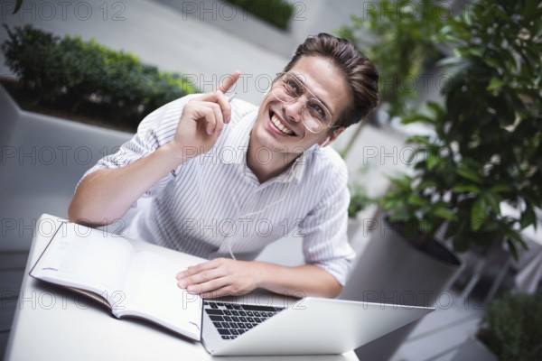 Happy handsome businessman mixes his break and job outdoors, businessman with headphones write some new ideas in notebook sitting in cafe