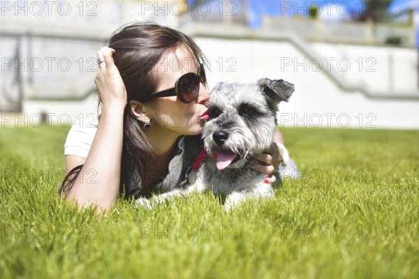 Pretty adult caucasian happy woman resting in the park on a sunny day with her beloved dog. Female lay on the grass smiling and looking at the camera