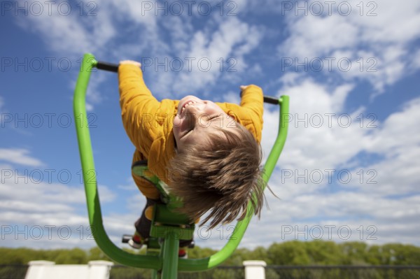 Funny little boy on a swing with his head down. Happy child on a walk. Ten year old boy against the background of the sky