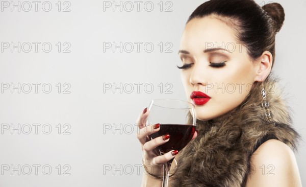 Beautiful woman with dark makeup and red lipstick posing on light grey background. Drinking glass of red wine, Toronto, Canada, North America