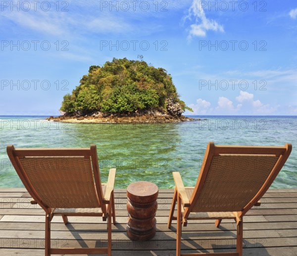 The charming landscape. A green island in a sea bay with emerald water. Two wooden chairs - on a wooden platform. The comfortable place to enjoy the beauty of the landscape