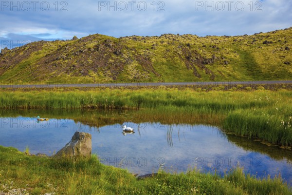 Small lake with thermal water. In the smooth surface of the water reflects the sky and clouds. Iceland in the summer
