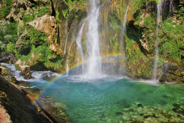Waterfall with rainbow, surrounded by rocks and green foliage under a clear sky, Topoljski Buk Kovacic Dalmatia Croatia