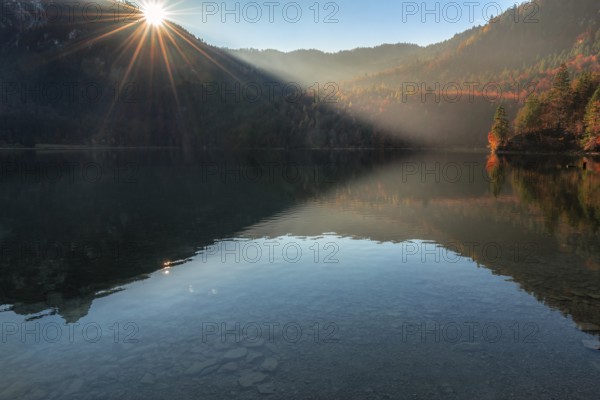Contemplative autumn landscape with wooded hills, autumn forest, and the Alpsee lake, on a sunny morning, near Fussen, in Bavaria, Germany, Europe