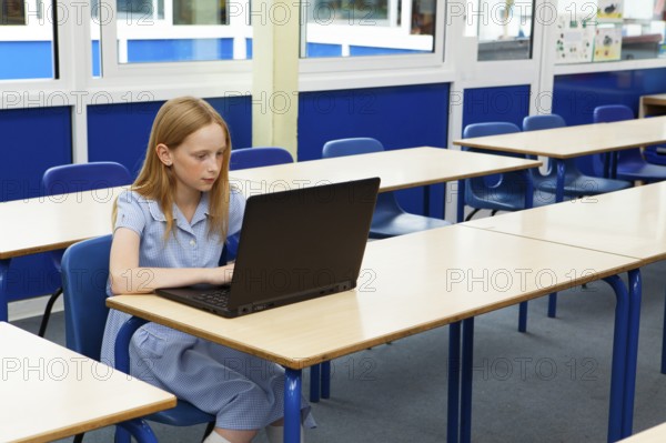 Primary school caucasian girl using a laptop in an empty classroom