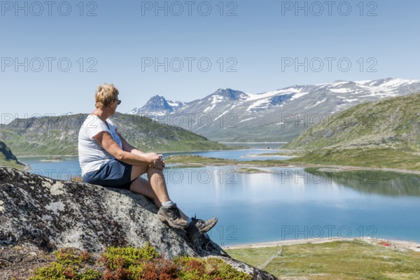 Adult woman sitting on a rock looking over the national park from bitihorn to stavtjedtet with lakes fjord and snow on the mountains