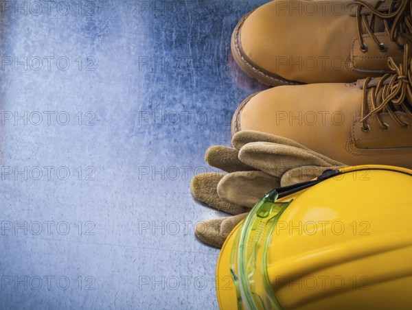 Protective leather gloves waterproof safety boots hard hat and plastic glasses on scratched metallic background construction concept