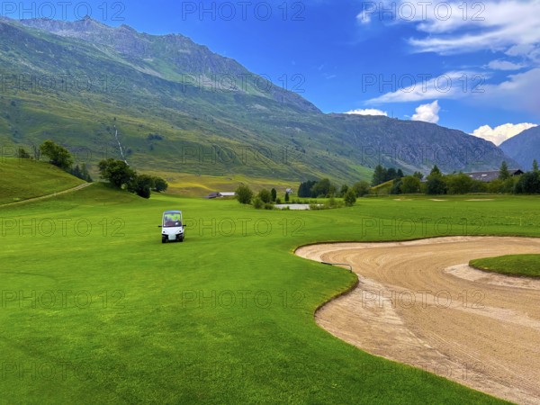 Beautiful Modern Luxury Golf Cart on Golf Course with Sand Trap and with Mountain View in the Swiss Alps in a Sunny Summer Day in Andermatt, Uri, Switzerland, Europe