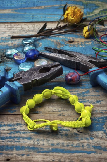 Beads, pliers, and other needlework accessories on outdated turquoise wooden background