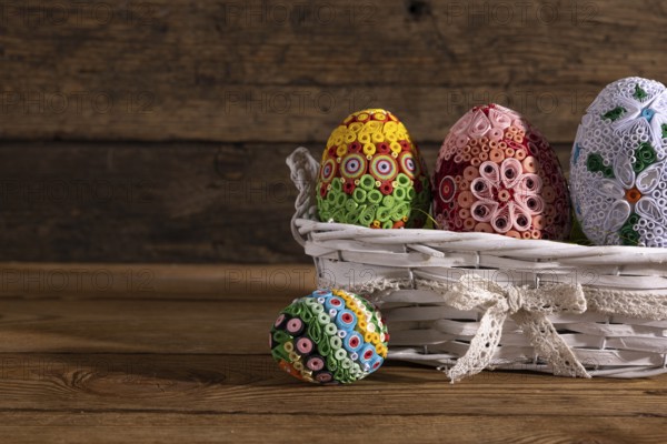 On a background of brown boards set a woven basket with colorful Easter eggs. Easter composition as decoration and symbol of the holiday