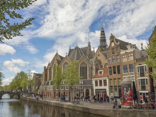 View of a canal with historic buildings and a church under a partly cloudy sky, Amsterdam, Netherlands