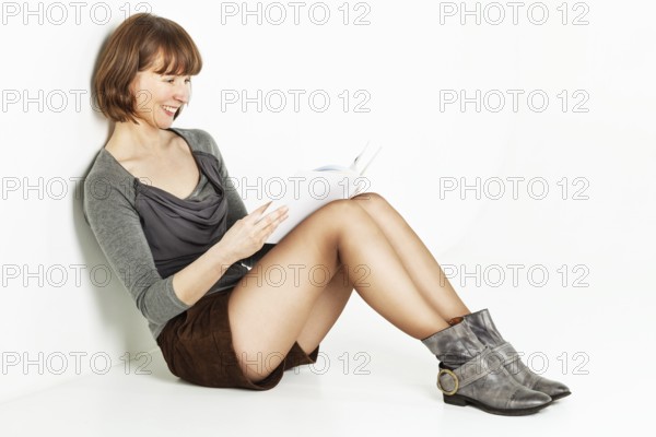 Smiling middle aged woman sitting on the floor with a book, Belgium, Europe