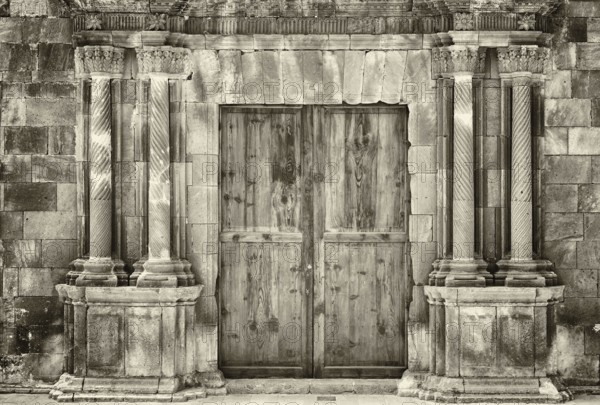 Monochrome sepia ancient wooden double doors in an old stone building with crumbling ornate columns surrounding the entrance