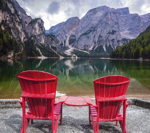Two comfortable red deck chairs on the shore of the lake. Water reflects the surrounding mountains and forest. The concept of walking and eco-tourism