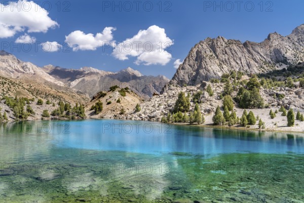 The beautiful mountain trekking road with clear blue sky and rocky hills and the view of Alaudin lake in Fann mountains in Tajikistan