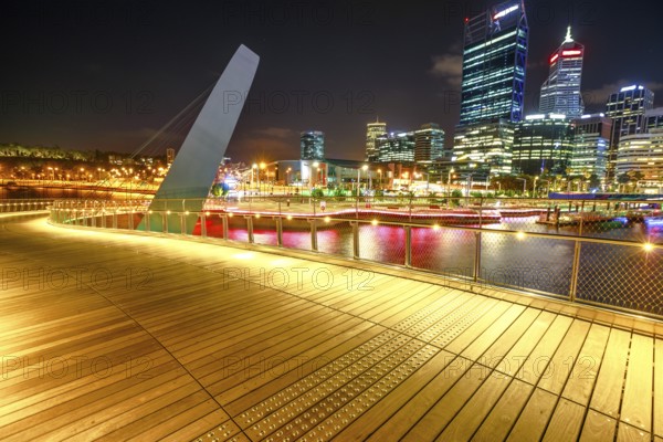 Wooden walkway of Elizabeth Quay pedestrian bridge illuminated by night at Elizabeth Quay marina, a new tourist attraction in Perth, Western Australia. Esplanade on background. Night scene, Perth, Australia, Oceania