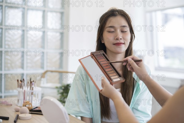 Makeup artist. Professional makeup artist working with beautiful young asian woman applying cosmetics by professional make up