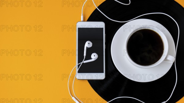 Cup of black coffee on vynil record. Copy space. Listening to music. Retro style. Podcast. Mobile phone with headphones