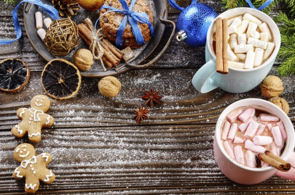 Flat lay Christmas background of two mugs of hot chocolate with marshmallows, spruce branch and tray with gingerbread man cookies on wooden table